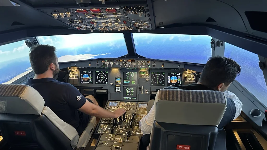 Two pilots at the controls of a SkyDynamics A320 FNPT II simulator flight deck